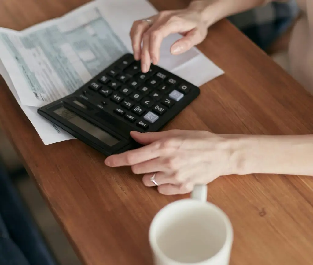 A woman uses a calculator to manage finances at home, focused on budget planning.